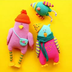 two knitted animals are sitting next to each other on a bright yellow surface, one is wearing a hat and the other has a scarf