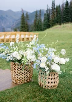 two baskets filled with white and blue flowers sitting on top of a grass covered field