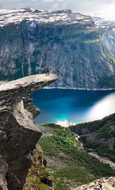 a person standing at the edge of a cliff overlooking a lake with mountains in the background