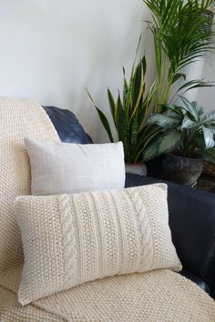 a couch with two pillows on top of it next to some plants and a potted plant