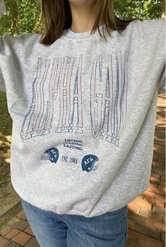 a woman wearing a gray shirt with the word gads on it, standing in front of some trees