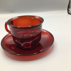 a red glass cup and saucer on a white table