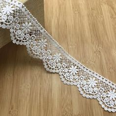 a white lace ribbon with flowers on it sitting on top of a wooden table next to a piece of cloth