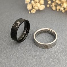 two wedding rings sitting next to each other on top of a gray surface with flowers in the background