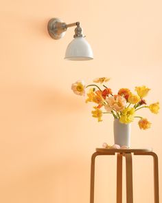 a white vase with yellow and red flowers on a table next to a light fixture