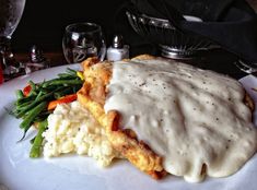 a white plate topped with meat covered in gravy next to mashed potatoes and green beans