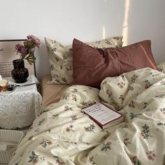 an unmade bed with pink flowers on it and a book sitting on the end table