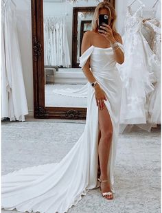 a woman taking a selfie in front of a mirror wearing a white dress and high heels