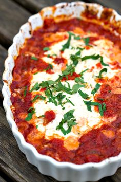 a pizza dish with sauce, cheese and herbs in it sitting on a wooden table