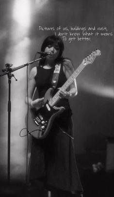 a woman standing in front of a microphone while holding a guitar