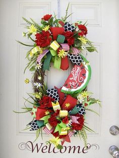 a welcome wreath is hanging on the front door with red flowers and green ribbon around it