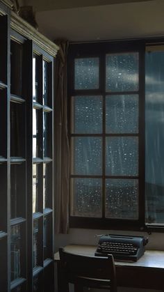 an old fashioned typewriter sitting in front of a window with rain drops on it