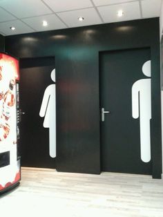 two men and a woman are standing in front of the restroom doors