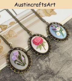 three necklaces with flowers on them sitting on top of a book page next to a window