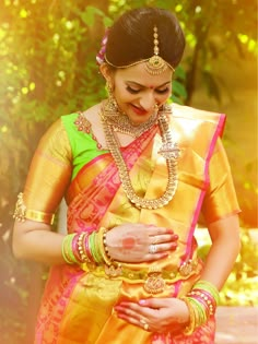 a woman in a yellow and pink saree holding her hands on her chest, looking down