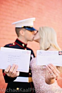 a man and woman kissing in front of a brick wall while holding letters to each other