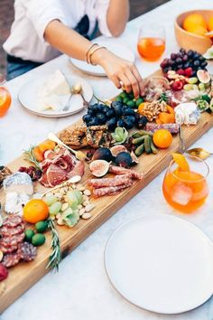 two people are serving food on a long wooden platter with oranges and grapes