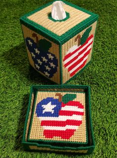 two pieces of cross - stitch are sitting on the grass, one has an american flag