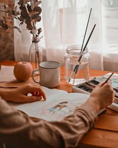 a person sitting at a table with an apple and watercolor pencils in front of them