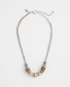 a silver and gold necklace on a white surface with some beads hanging from the chain