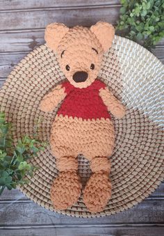 a crocheted teddy bear sitting on top of a basket next to a plant