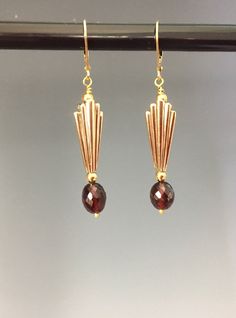 "If you love the look of Art Deco design you will love these beautiful earrings! We first start with lovely, clear, deep red, faceted Garnet gemstones with an oval shape. Adorning the gemstone is a light bronze charm with the quintessential Art Deco fan shape. These charms have a nice weight and feel with a finish that looks more like vintage gold than bronze. Gold Fill lever back ear wires complete the look for wonderful comfort and security. The earrings hang 2-inches. These make a perfect gif Art Deco Jewelry 1920s, Art Deco Inspired Jewelry, Gold Art Deco Earrings, Gatsby Jewelry, Art Deco Jewellery, 1920s Jewelry, Spinel Jewelry, Art Deco Fan, Perfect Gif