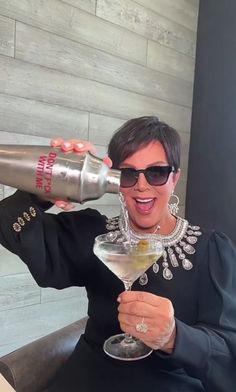 a woman sitting in a chair holding a martini glass with a silver shaker on top of it