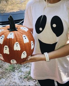 a person holding a pumpkin with ghost faces on it and a car in the background