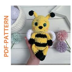 a hand holding a yellow and black knitted stuffed animal with flowers in the background