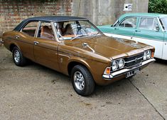 two old cars parked next to each other in a parking lot with brick walls behind them