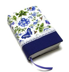 a book with blue flowers and butterflies on it, sitting on a white tablecloth