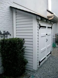 a white building with a black sign on it's side and a green bush next to it