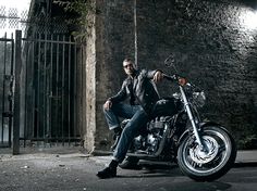 a man sitting on top of a motorcycle in front of a brick wall and gate