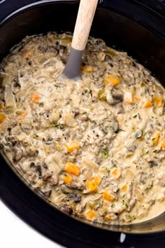 a crock pot filled with mushroom soup and carrots is being stirred by a wooden spoon