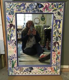 a woman taking a selfie in front of a mirror with flowers painted on it