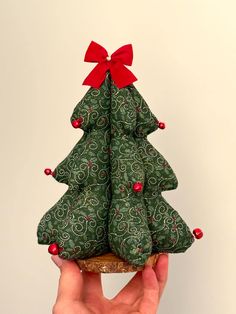 a hand holding a small green christmas tree ornament with red bows on it