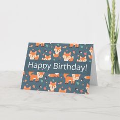 a happy birthday card with foxes and leaves on it, sitting next to a vase