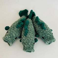 three green crocheted stuffed animals sitting on top of each other in front of a white background