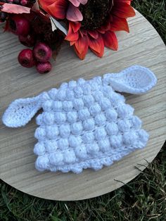 a crocheted sheep is sitting on a table next to some flowers