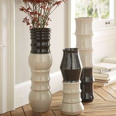 three vases with flowers in them sitting on a wooden floor next to a window