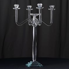 a glass candelabra with four candles on it's stand, in front of a black background