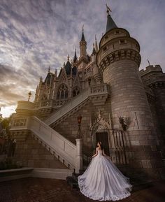 a woman is standing in front of a castle with stairs leading up to her wedding dress