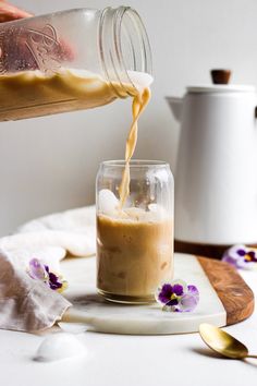 someone is pouring something into a glass with some flowers on the table next to it