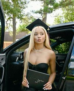 a woman sitting in the back seat of a car holding a book and wearing a graduation cap