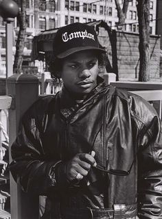 a black and white photo of a young man wearing a leather jacket, hat and jeans