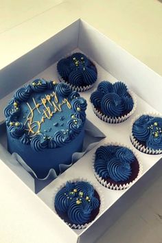 four blue cupcakes in a white box with happy birthday written on them