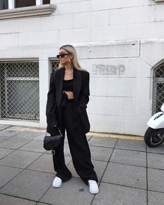 a woman standing in front of a white building wearing black pants and a blazer