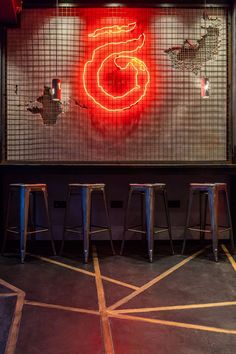 three stools sit in front of a neon sign