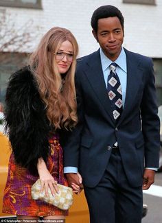 a man in a suit and tie walking next to a woman wearing a fur stoler