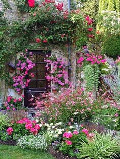 a garden with lots of flowers and plants growing on the side of it, next to a stone building